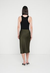Black tank top paired with a knee-length olive green satin skirt. The outfit features a smooth texture and fitted design, complemented by black heeled mules.
