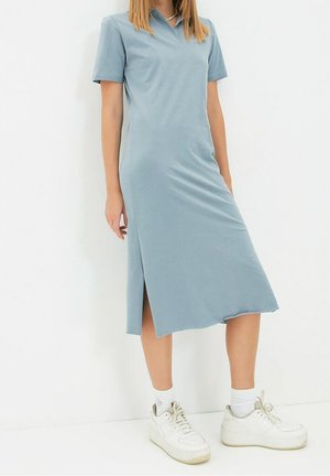 Lyseblå, kortærmet kjole med krave og sideslid, lavet af glat stof. Sammen med hvide, teksturerede sneakers og ankelstrømper.