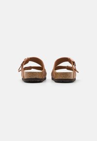 Brown leather sandals with an adjustable strap, cork footbed, and textured rubber sole. Features a bow accent near the heel.