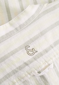 Tessuto di lino leggero con strisce verdi e bianche alternate, caratterizzato da un decorativo "&" ricamato con filo metallico.