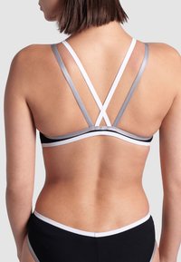 Černé bikiny s kříženými ramínky v šedé a bílé. Texturovaná látka a kontrastní lemování zdůrazňují design. Pohled zezadu ukazuje detaily ramínek.