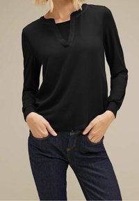 Svart långärmad blus med V-ringning och subtila skimrade detaljer. Mjuk, flödande tyg kombinerad med mörka denimjeans.