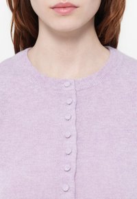Cárdigan lila hecho de una suave tela de punto, con un escote redondo y siete botones texturizados en la parte delantera, con una textura suave y uniforme.