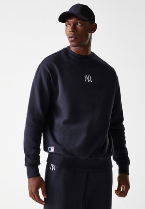 Marineblaue Sweatshirt aus weichem Material, mit einem silbernen gestickten Logo auf der Brust und einem weißen MLB-Label am Saum.