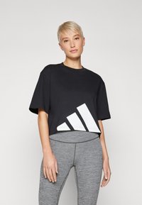Fekete crop póló, amely pamutból k�észült, az alján egy nagy fehér geometrikus mintával. Szürke leggings-szel párosítva.