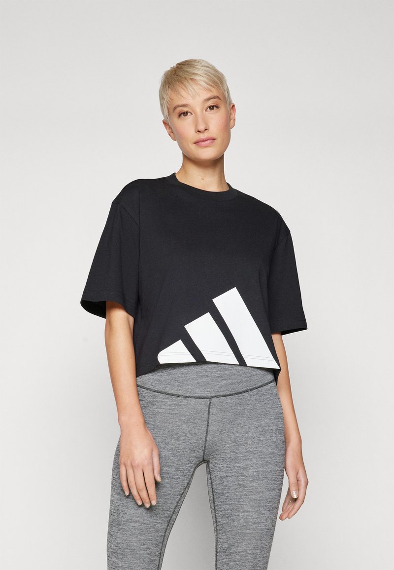 Fekete crop póló, amely pamutból készült, az alján egy nagy fehér geometrikus mintával. Szürke leggings-szel párosítva.