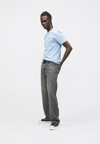 Világoskék rövid ujjú póló kis logóval, szürke farmerral és fekete, fehér talpú tornacipővel párosítva. Laza, kényelmes stílus.