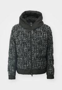 Padded jacket in black and white tweed fabric with a high collar, zip closure, and two front pockets. Textured pattern throughout.
