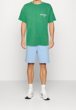 Green cotton t-shirt with "SAN DIEGO" print on the chest, paired with light blue shorts and white sneakers with gray accents.
