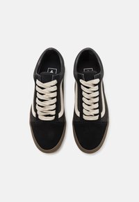 Sorte og beige ruskinds sneakers med rund tå, hvide snørebånd, fremtrædende sidestriber og en tekstureret gummisål.