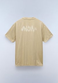 Camiseta de algodón beige, de gran tamaño y de manga corta. Presenta un gráfico blanco de árboles y texto en la parte posterior. Textura suave, cuello redondo.