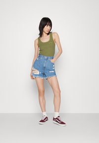 Top sin mangas acanalado en verde oliva, pantalones cortos de mezclilla desgastados de tiro alto con dobladillo desflecado y zapatillas burdeos con acentos en blanco.