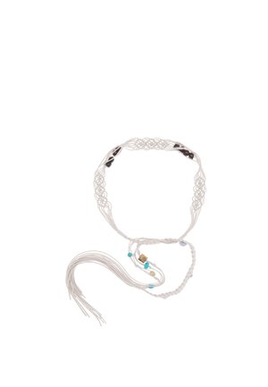 Cinturón de macramé trenzado blanco con cuentas negras, turquesas y beige y flecos colgantes sobre un fondo blanco.