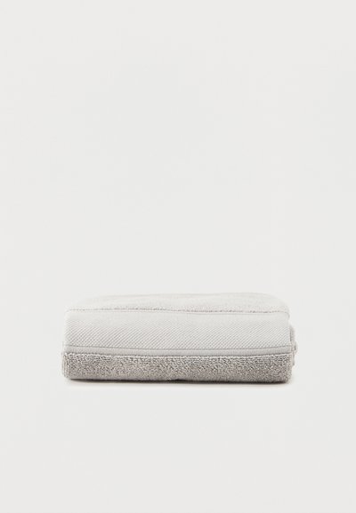 Διπλωμένη πετσέτα σε ανοιχτό γκρι χρώμα με στρώματα υφάσματος που έχουν υφή και λεία επιφάνεια, σε απλό λευκό φόντο.