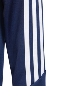 Calças de desporto azul-marinho com três riscas verticais brancas ao longo do lado, feitas de um tecido texturizado com um design de perna afunilada.