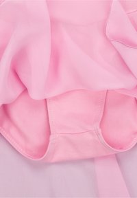 Vêtement rose pâle avec un tissu doux et transparent superposé sur une base en coton uni. Texture lisse avec un léger éclat, bords incurvés visibles.