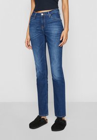 Jeans in denim blu con taglio a gamba dritta, cinque tasche e chiusura anteriore con bottone e zip. Tessuto strutturato con leggere sfumature.