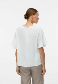 Blouse blanche à manches courtes avec une coupe décontractée, présentant un col rond et un petit détail en forme de clef à l'arrière. Texture lisse et légère.