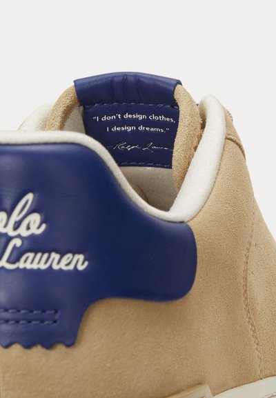 Beige mockasinliknande sneaker med blått läder på hälen, vit Polo Lauren-logotyp och inneretikett med texten "Jag designar inte kläder, jag designar drömmar."
