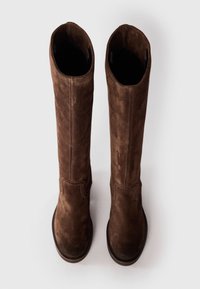 Bottes en daim marron jusqu'au genou avec une texture lisse, une ouverture rectangulaire et un minimum de détails de couture sur les côtés. Semelles plates.