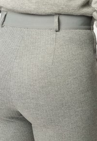 Gros plan sur un pantalon gris clair à motif chevrons avec une ceinture grise assortie et un pull en maille rentré à la taille.