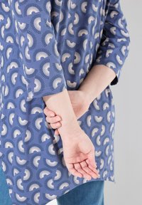 Blaue Tunika mit einem sich wiederholenden weißen und marineblauen Fächer-Muster, mit dreiviertel Ärmeln und lockerem Schnitt, kombiniert mit hellblauem Denim.