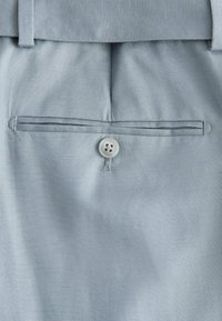 Light gray dress pants back pocket with single button closure and belt loops on textured fabric.