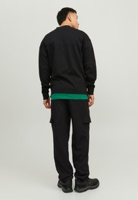 Črna kapuca z okroglo odprtino, položen na zeleni srajci. V kombinaciji s črnimi cargo hlačami, ki imajo žepke, in črnimi športnimi copati.