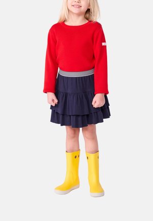 Roter Strickpullover, marineblaue Rüschensocke mit gestreiftem Bund und gelbe Gummistiefel mit Ausschnitten.