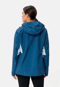 Giacca impermeabile blu con cappuccio, caratterizzata da pannelli laterali in blu chiaro a contrasto e una texture liscia. Include polsini regolabili.