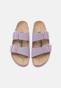 Ζευγάρι λιλά σανδάλια με δύο ρυθμιζόμενα λουράκια με αγκράφες και ταμπά σουέτ πάτους, εμφανιζόμενα από πάνω σε λευκό φόντο.