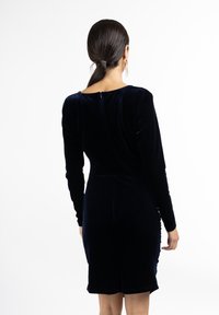 Rochie din catifea bleumarin, cu mâneci lungi, siluetă ajustată și închidere cu fermoar la spate. Textura fină și luciul subtil sunt detalii notabile.