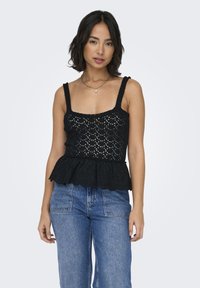 Top peplum in crochet nero con scollatura quadrata e spalline larghe. Pattern in pizzo strutturato con orlo ondulato. Abbinato a jeans in denim a vita alta.