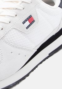 Λευκό αθλητικό παπούτσι με πλέγμα και υφές σουέντ, με λογότυπο Tommy Jeans σε κόκκινο, άσπρο και μπλε στο πλάι και μαύρη και λευκή σόλα.