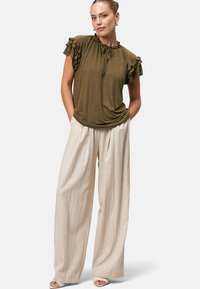 Olive green short-sleeve top with ruffled edges, paired with loose, cream-colored wide-leg pants. The outfit features a drawstring neckline.