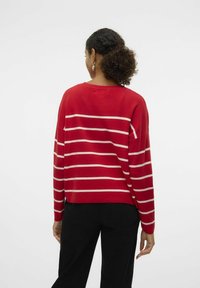 Rood gestreepte trui met crèmekleurige horizontale strepen, zachte textuur, relaxte pasvorm, ronde halslijn en doorgeschoven schouders. Gecombineerd met zwarte broek.
