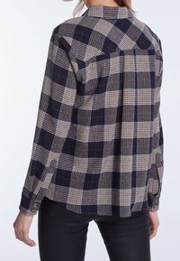 Chemise à manches longues en tartan bleu marine, beige et bordeaux. Dotée d'un col classique, de poignets à boutons et d'un pli au dos pour plus de liberté de mouvement.