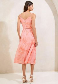 Floral-patterned pink midi dress featuring thin straps, a fitted bodice, and a flared hem, paired with strappy white high heels.
