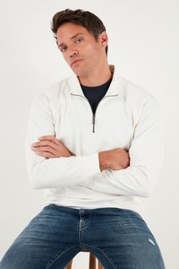 Valge veerandzipperiga pulli, millel on kõrge krae ja hõbedane tõmblukk; kantud tumesinise särgi üle. Kombineeritud helesiniste teksadega, millel on kerge kulumine.