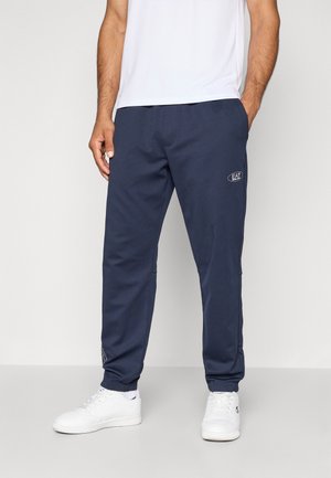 Pantaloni felpa navy con elastico in vita, tasche laterali e polsini affusolati; presenta un dettaglio del logo sulla coscia; tessuto liscio e traspirante.