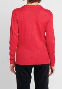 Rode gebreide trui met lange mouwen, geribbelde halslijn en manchetten, met een gladde textuur en een relaxte pasvorm, gedragen over een donkere broek.