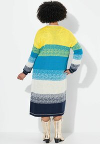 Gestricktes langes Kleid mit mehrfarbigen Streifen in Gelb, Türkis, Weiß und Marineblau. Hat eine lockere Passform und gerippte Bündchen. Getragen mit metallischen Stiefeln.