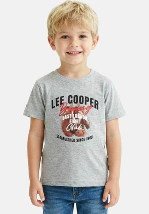 Jeune garçon souriant aux cheveux blonds portant un t-shirt gris avec des gants de boxe rouges et le texte "Lee Cooper Boxing East London Fight Club."