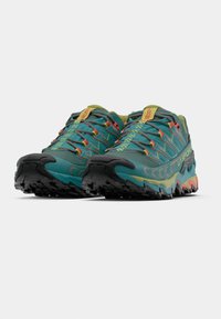 Sapatos de trail running em teal com detalhes contrastantes em amarelo e vermelho. Superior em malha, sola com padrão agressivo e biqueira reforçada para durabilidade.