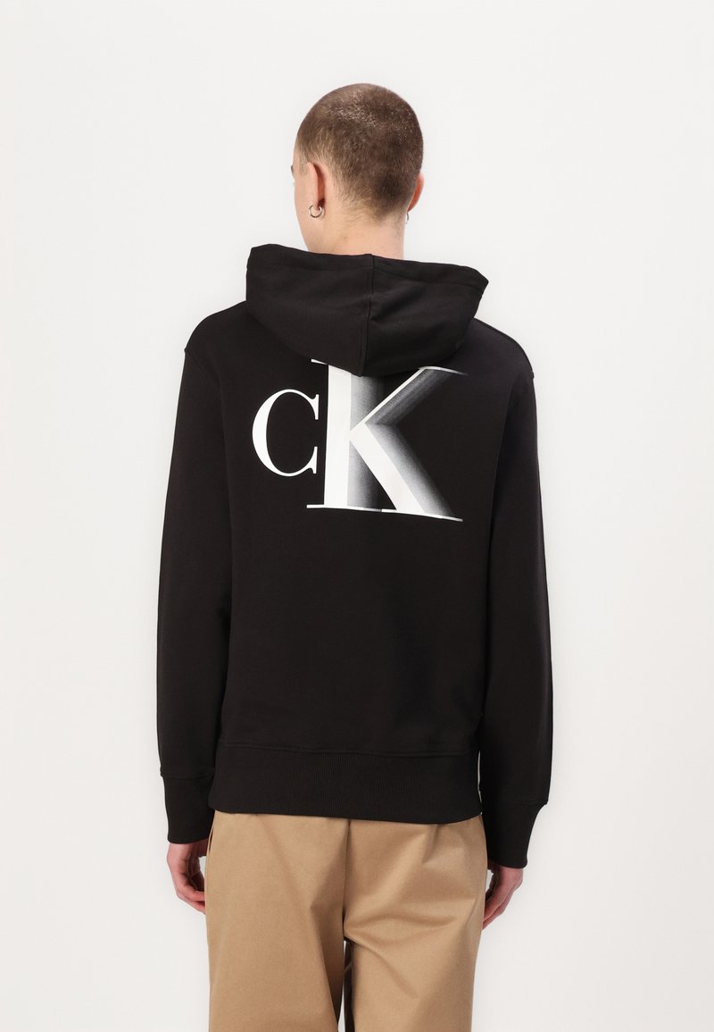 Felpa nera con cappuccio caratterizzata da un grande logo "CK" bianco sul retro, con una texture liscia e morbida e una vestibilità comoda.