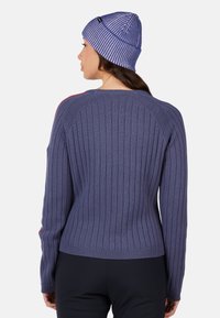 Fioletowy sweter w prążki z długimi rękawami, okrągłym dekoltem i subtelnymi czerwonymi akcentami po bokach. Uzupełniony dopasowaną fioletowo-białą czapką w paski.