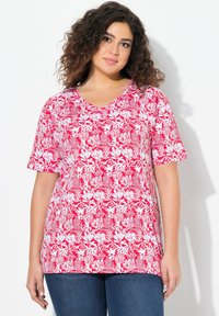 Červená a bílá květinová halenka s krátkým rukávem ve V výstřihu, s volným střihem, opatřená listovým vzorem na jemné látce, nosená s modrými džíny.