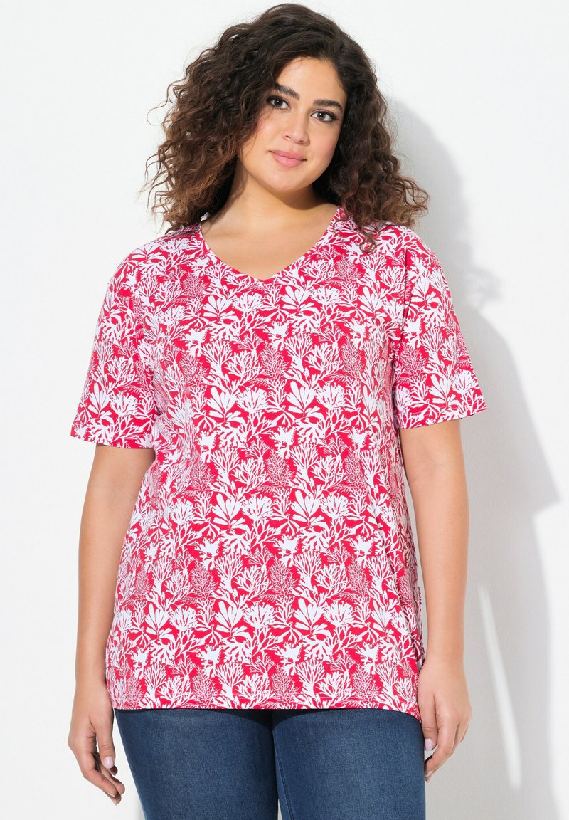 Červená a bílá květinová halenka s krátkým rukávem ve V výstřihu, s volným střihem, opatřená listovým vzorem na jemné látce, nosená s modrými džíny.