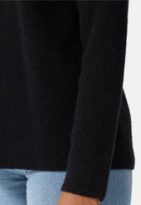 Maglione nero lavorato a maglia con tessuto testurizzato. Caratterizzato da maniche lunghe e una vestibilità rilassata, abbinato a jeans in denim blu chiaro.