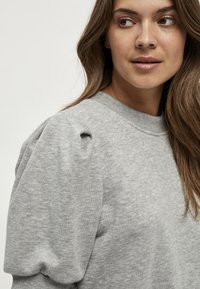 Grå sweatshirt med texturerade puffärmar och ribbade ärmslut. Tyget har en mjuk yta och erbjuder en avslappnad och komfortabel passform.